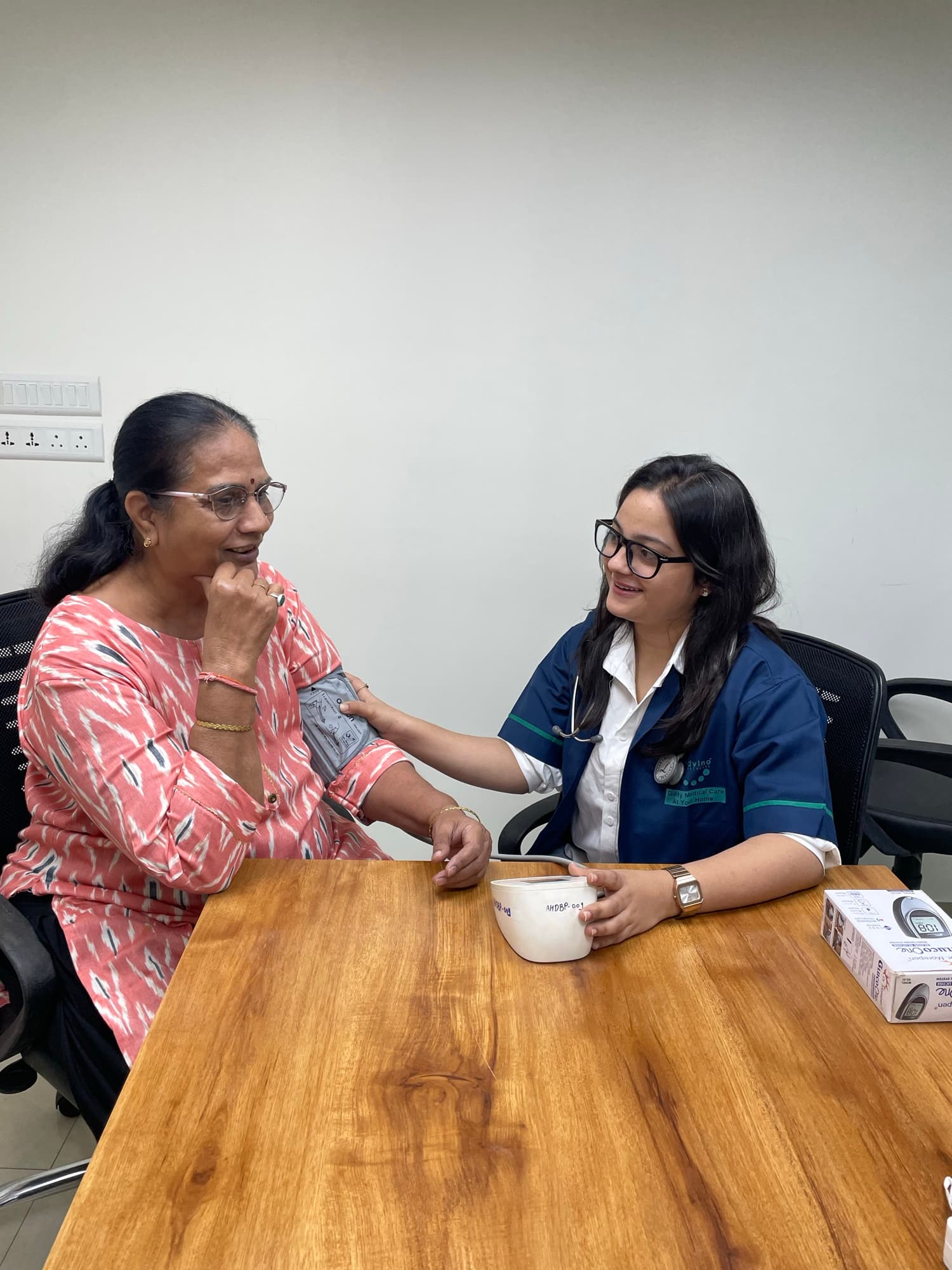 An Advino nurse in uniform sitting with an elderly woman at a table during a routine health check.